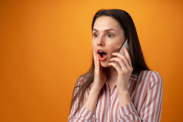 Studio photo of young woman talking on the phone against yellow