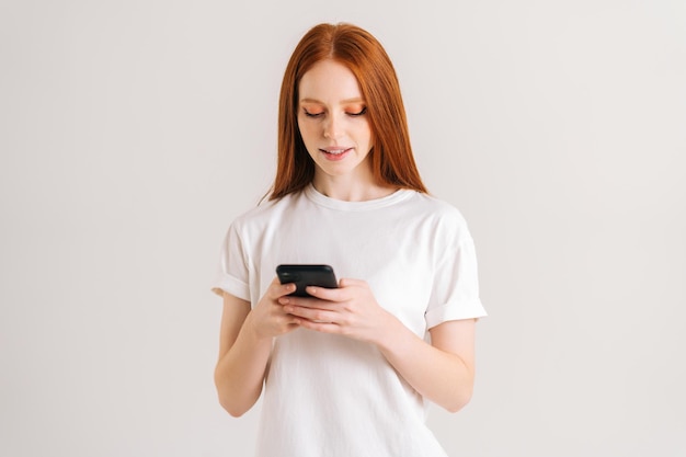 Studio portrait of attarctive young woman typing online message using mobile phone on white isolated