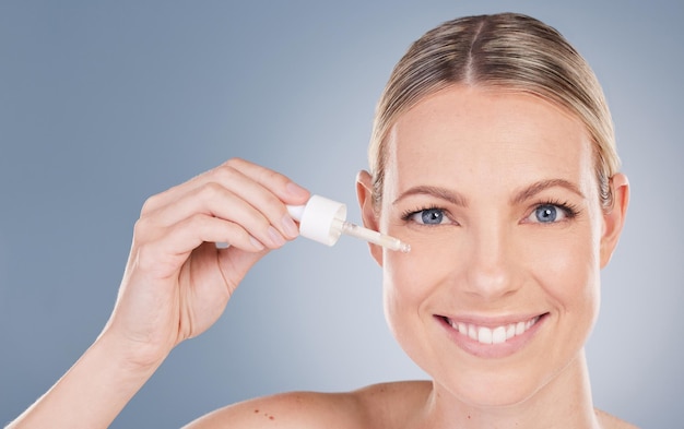 Studio portrait of an attractive young woman applying facial serum against a grey background