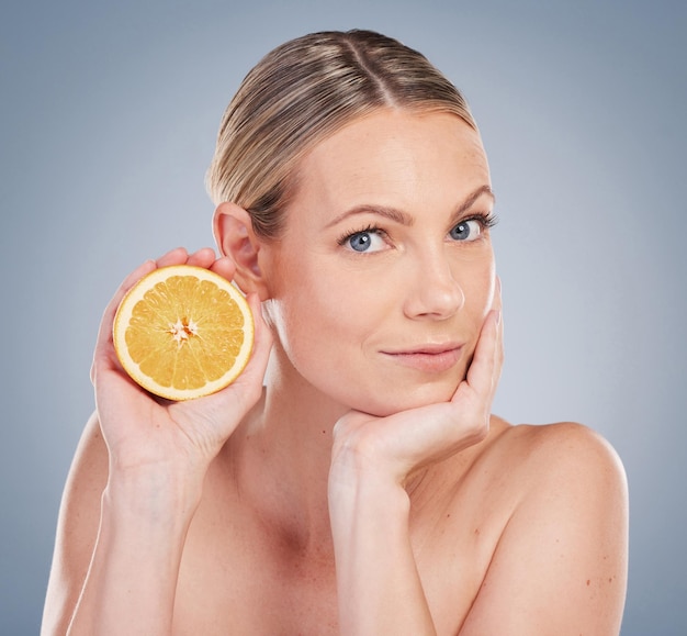 Studio portrait of an attractive young woman posing with half an orange against a grey background