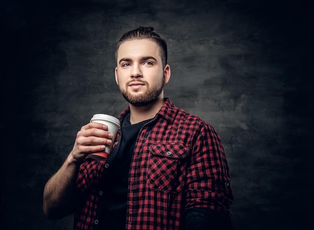 Studio portrait of bearded hipster male dressed in a fleece shirt holds coffee paper cup.