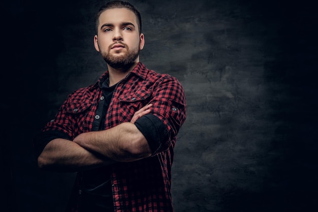 Photo studio portrait of bearded hipster male with crossed arms, dressed in a red fleece shirt over grey background.