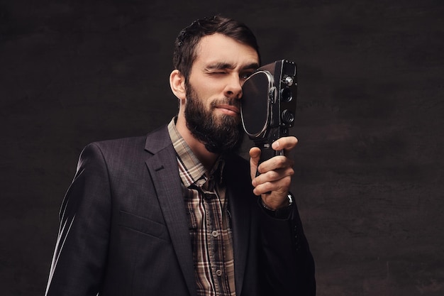 Ritratto in studio di uomo barbuto che indossa un abito classico in possesso di una fotocamera retrò, facendo una foto. isolato su uno sfondo scuro.