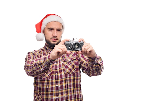 Studio portrait of bearded man wearing santa hat holding a retro camera, making a photo. Isolated white background