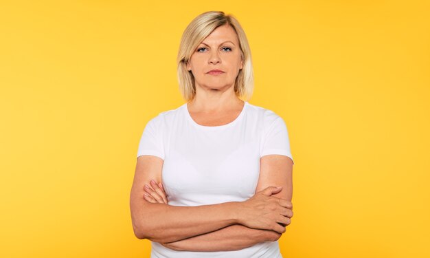 Studio portrait of beautiful serious senior woman isolated on yellow background and looks on camera