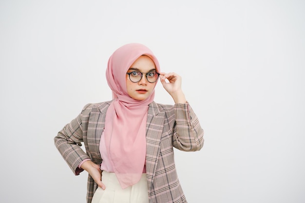 白い背景の上でカメラにポーズをとり ⁇ 眼鏡をかぶったピンクのヒジャブを着た美しい若いイスラム教徒のビジネスウーマン ⁇ のスタジオポートレート