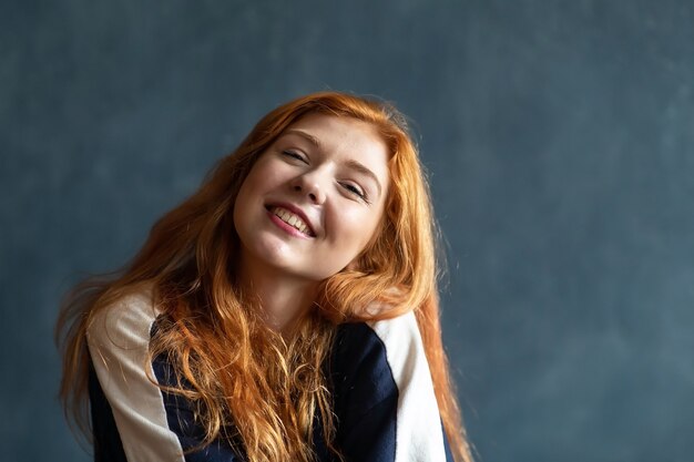 Studio portrait of beautiful young red-haired woman. Emotions of a girl on blue background. Map of emotions