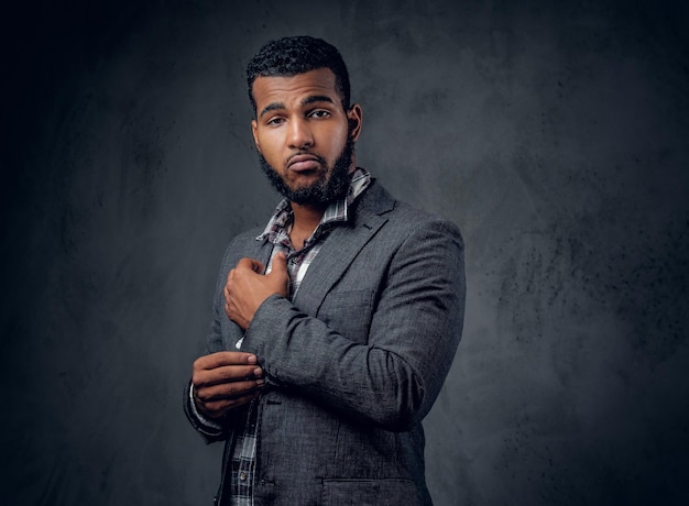 Studio portrait of Black hipster male dressed in a fleece shirt and a jacket posing over grey artistic background.