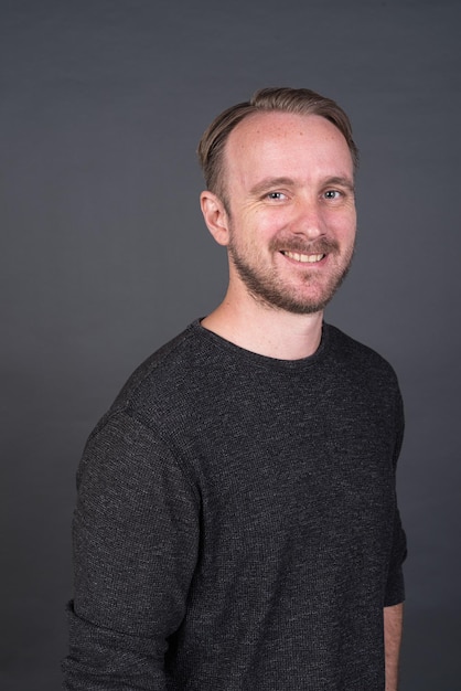 Studio portrait of blonde Caucasian man smiling against gray background