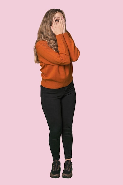 Photo studio portrait of a blonde caucasian woman blink through fingers frightened and nervous