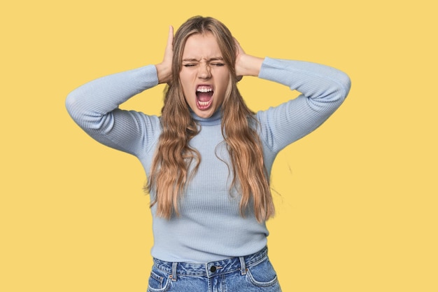 Photo studio portrait of a blonde caucasian woman covering ears with hands