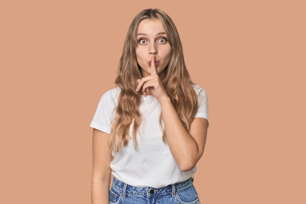 Photo studio portrait of a blonde caucasian woman keeping a secret or asking for silence