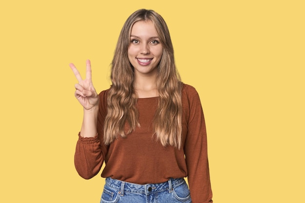 Studio portrait of a blonde Caucasian woman showing victory sign and smiling broadly