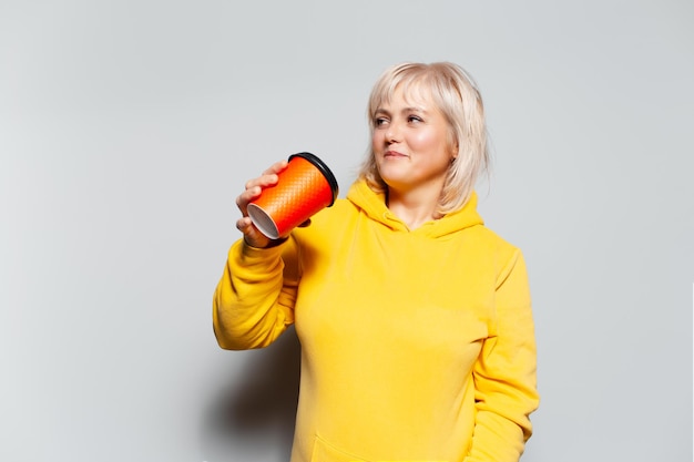 Studio portrait of blonde woman drinking coffee from paper cup on white background