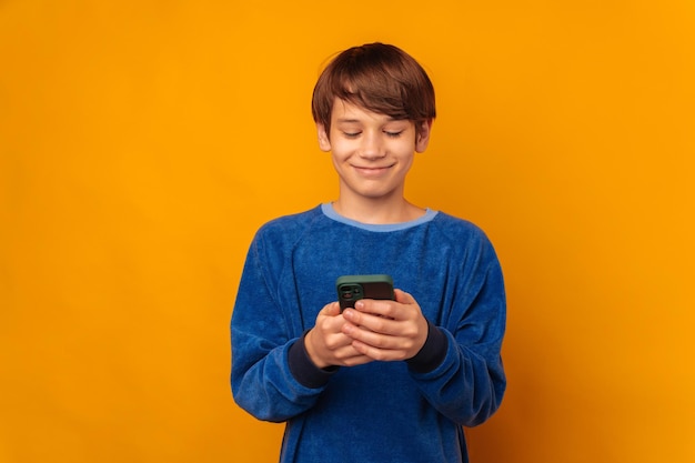 Studio portrait of a cheerful teen boy is typing a message on his phone