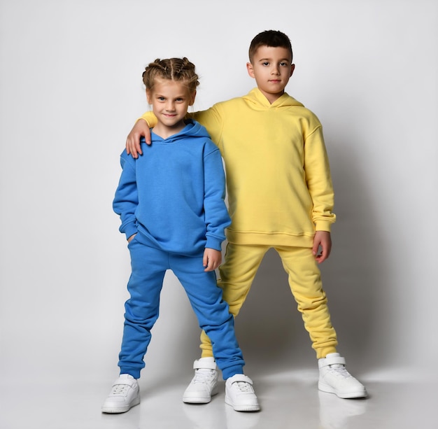 Studio portrait of a cool little boy and girl dressed in stylish bright sports suits with sweatshirts and pants on a white background Children's sports style concept Banner