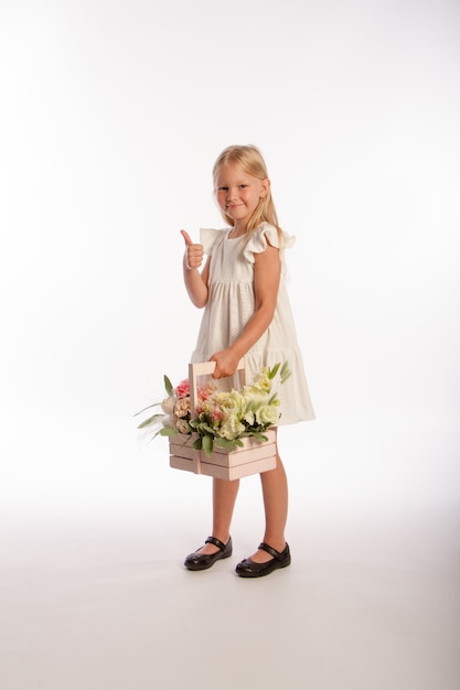 Studio portrait of cute blonde girl in white dress with wooden basket of flowers,