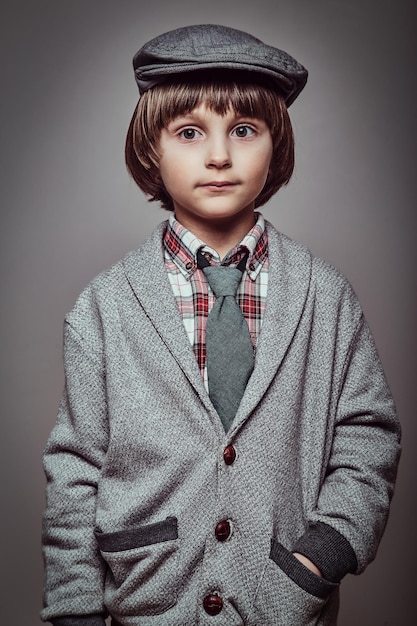 Studio portrait of a cute Caucasian schoolboy wearing elegant clothes holds hands in pockets