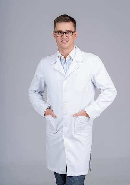 Studio portrait of a doctor or medical specialist. Standing with hands in pockets. Man in scrubs. Gray background.