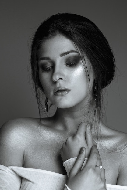 Studio portrait of elegant brunette woman with glowing skin and naked shoulders. Monochrome color