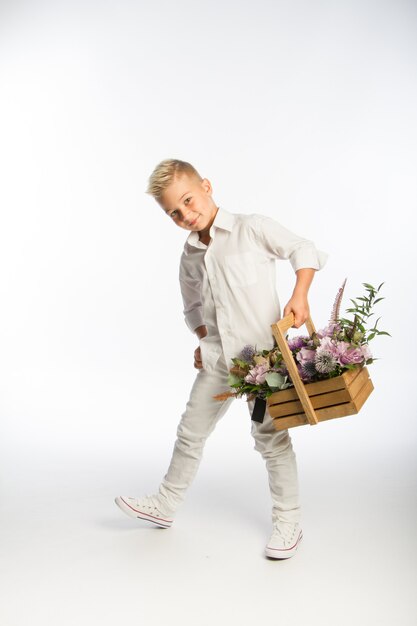 Studio portrait of fashionable blond caucasian boy with wooden basket of flowers, white wall, copy space