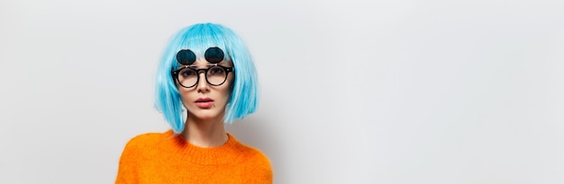 Studio portrait of fashionable pretty girl with blue hair wearing black sunglasses and orange sweater on white background. Panoramic banner photo with copy space for text.