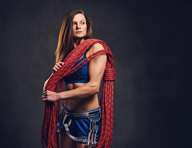 Studio portrait of female free clamber holds, climbing rope over grey background.