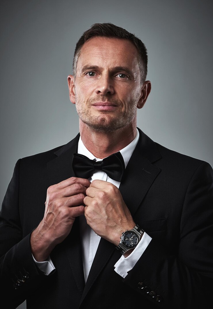 Photo studio portrait of gentleman in tuxedo fixing tie and serious isolated on grey background luxury fashion and and man with wealth success and celebrity actor style date for valentines day
