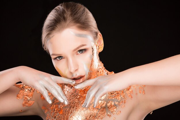 Ritratto in studio di un'affascinante modella bionda con una lamina dorata sulle spalle e sul viso