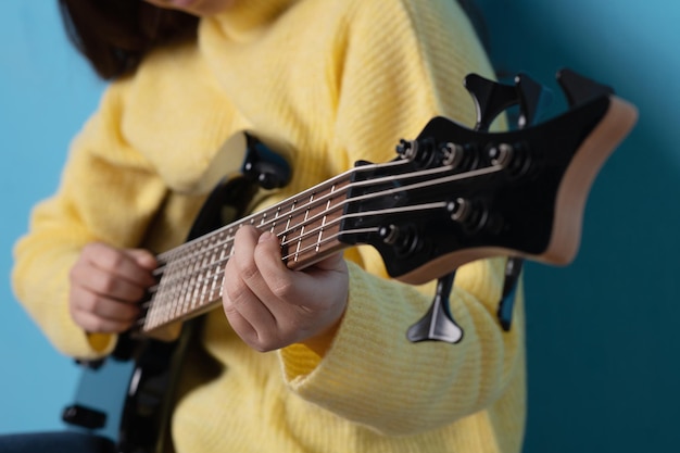 Studio portrait of the hands of a woman playing an electric\
guitar with a blue background