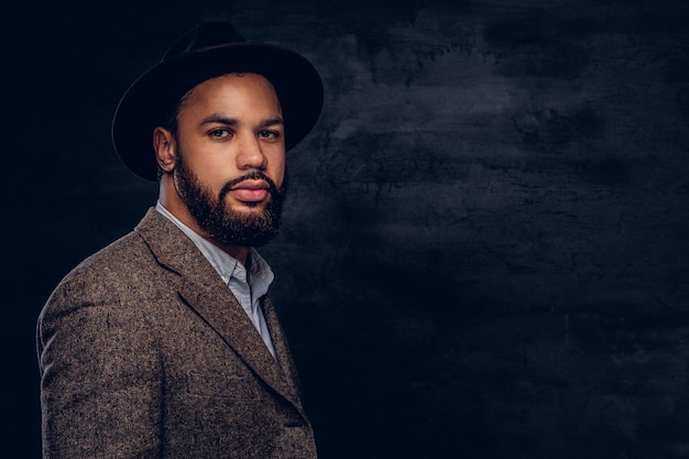 Photo studio portrait of handsome afro-american male in an elegant brown jacket and hat. isolated on a dark background.