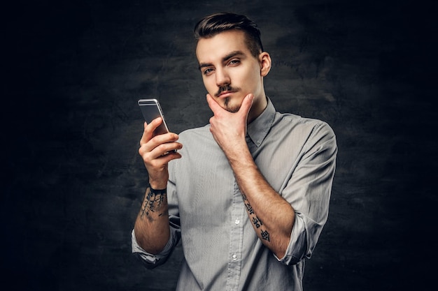 Studio portrait of handsome bearded hipster male with a tattoo on his arm using a smartphone.