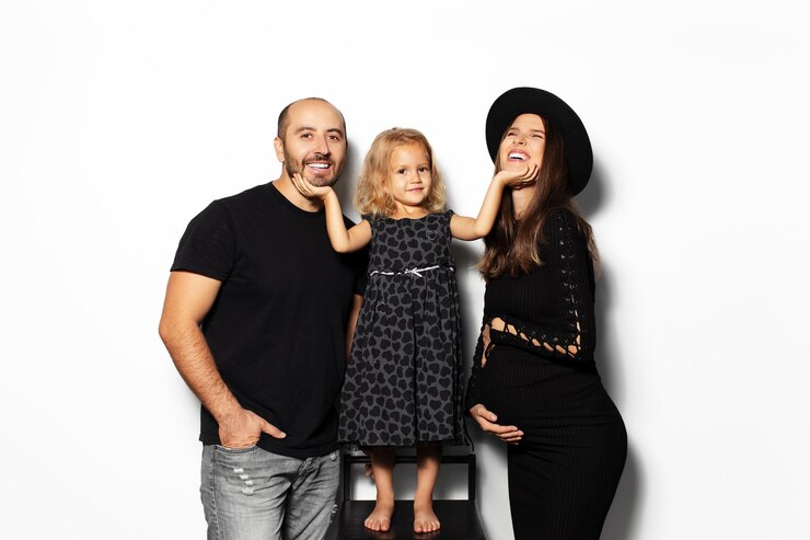 Studio portrait of happiness family of three dressed in black pregnant mother daughter and father isolated on white background