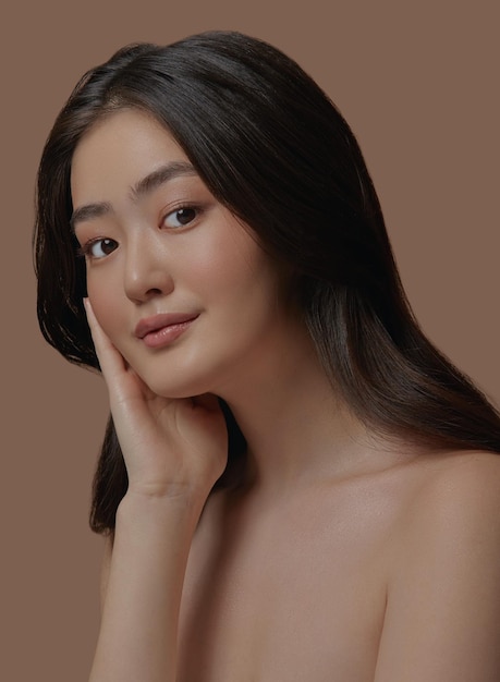 Studio portrait of happy Asian woman face with natural skin touching her face on beige