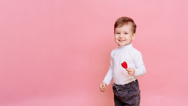 Studio portrait of a happy boy with a heart-shaped lollipop.