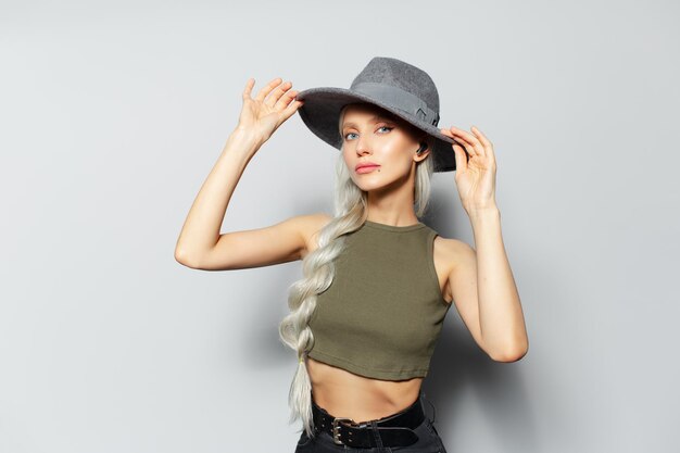 耳にワイヤレス イヤホンで幸せなかなり金髪の女の子のスタジオ ポートレートは、白い背景の上の彼女の帽子を調整します