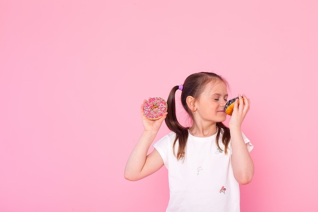 Studio portrait of a little girl holding a donut and smelling tasty flavour. Isolated on pink wall.