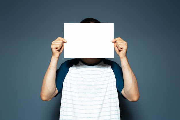 Photo studio portrait of man holding empty horizontal paper board on face copy space blue background