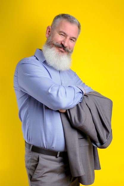 Studio portrait mature bearded man in gray business suit looking to camera, work profession lifestyle, yellow background.