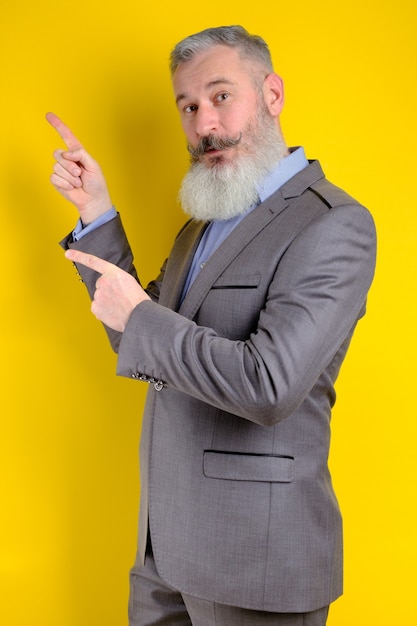 Studio portrait mature businessman dressed in gray suit points aside, I choose you this, yellow background