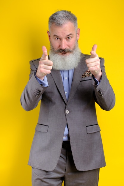 Studio portrait mature businessman dressed in gray suit points to camera, i choose you concept, yellow background