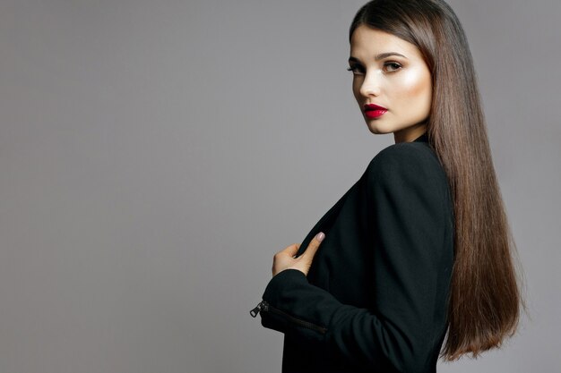 光沢のある髪と赤い唇を持つ素晴らしい女性のスタジオポートレートは黒いジャケットを着ています。空きスペース