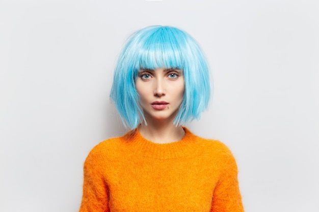 Photo studio portrait of pretty young girl against white background. wearing orange sweater and blue wig.