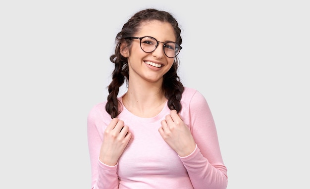 Studio portrait of pretty young woman smiling broadly wearing casual outfit and round eyeglasses Caucasian brunette female in pink blouse posing over white studio wall People and emotions concept