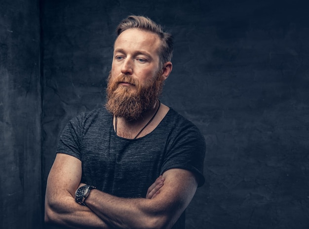 Studio portrait of redhead bearded hipster male with crossed arms over grey background.