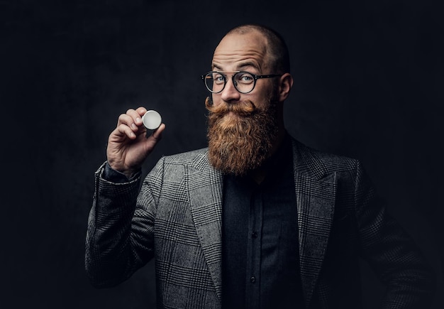 Studio portrait of redhead bearded male in vintage eyeglasses dressed in a wool jacket.