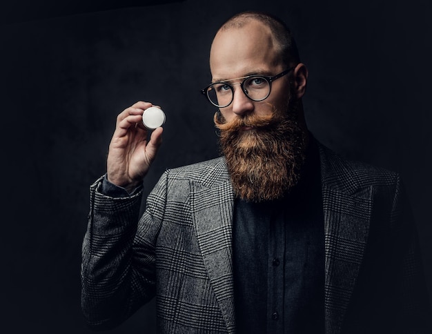 Studio portrait of redhead bearded male in vintage eyeglasses dressed in a wool jacket.