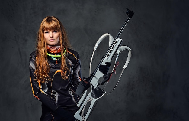 Ritratto in studio di una campionessa di biathlon rossa tiene una pistola su sfondo grigio.