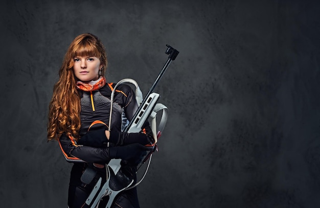 Studio portrait of a redhead female Biathlon champion holds a gun over grey background.