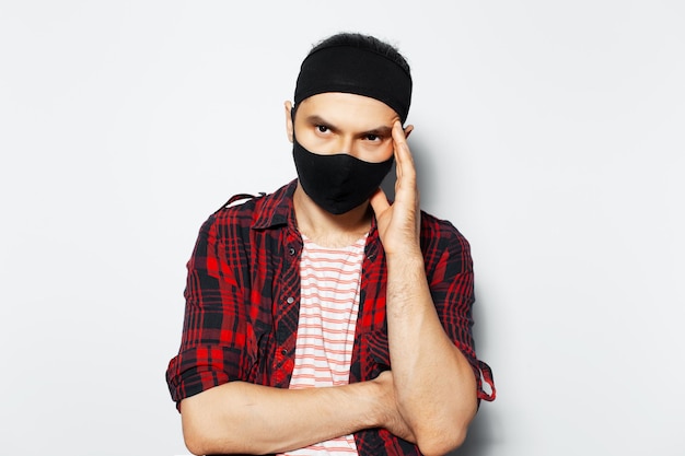 Studio portrait of sad man wearing black protective mask have headaches keeps hand on head on white background